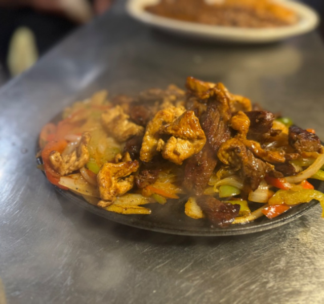 Sizzling combination fajitas with chicken, grilled steak, onions, and bell peppers on a cast-iron skillet