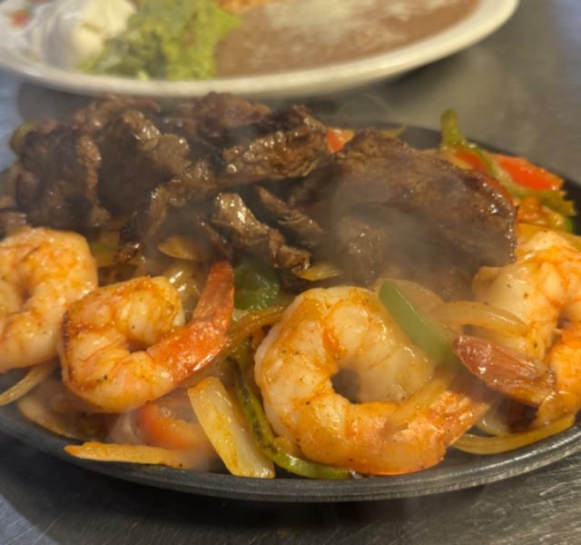 Sizzling vallarta fajitas with grilled steak, shrimp, onions, and bell peppers on a cast-iron skillet by La Tapatia