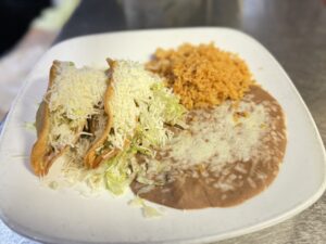 Two crispy tacos filled with cheese, lettuce, and mild red salsa served on a white plate