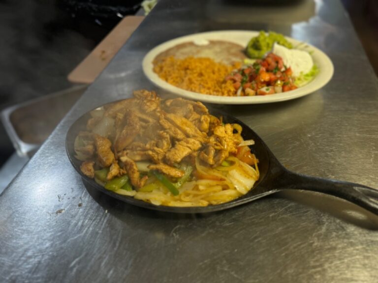 Grilled chicken fajitas with onions and bell peppers on a cast-iron skillet and another dish aside